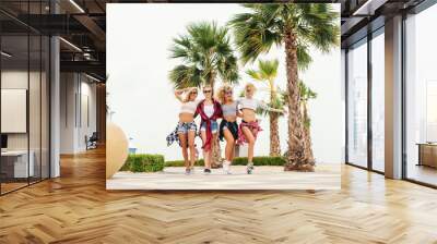 Four multicultural teenage girlfriends walking near beach. Palm trees in background. Wall mural