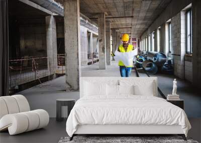 Full length of construction worker in work wear walking in building in construction process and looking at blueprints.a Wall mural