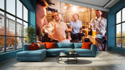 Handsome man drinking a glass of water in the local pub while his friends laughing with a beer in front. Wall mural