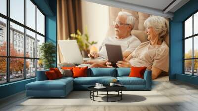 Happy senior couple sitting in bedroom and using technologies. Wall mural