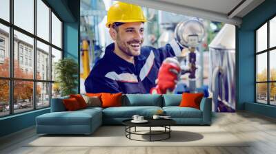 Hardworking smiling blue collar worker in protective working suit and with helmet adjusting temperature on boiler while standing in factory and holding lamp. Wall mural