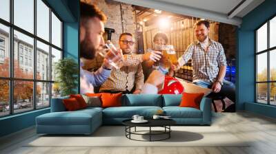 Joyful male friends clinking with draft beer in front of their friend while drinking water and holding motorcycle helmet in the local bar. Wall mural