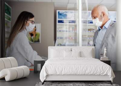 Making a prescription in a pharmacy and paying the bill with a card, selling medicines. A mature man swipes a card and pays for medications to pharmacists. Protective face mask during corona virus Wall mural