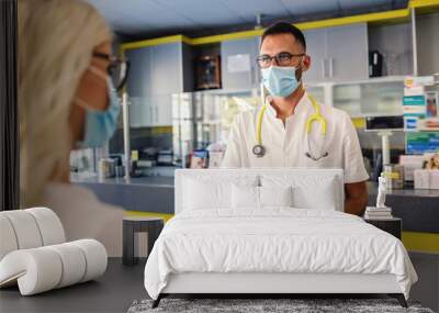 Medical worker in sterile uniform, with rubber gloves and face mask on giving corona virus test results to a female patient. Wall mural