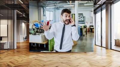 Nervous caucasian bearded graphic engineer talking on the phone and shouting. Printing shop interior. Wall mural