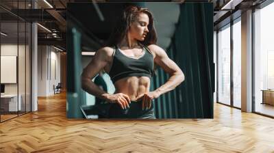 Portrait of beautiful Caucasian female bodybuilder posing with hands on hips in gym and looking down. Sore today. strong tomorrow. Wall mural