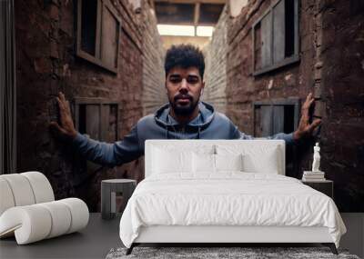 Portrait of focused motivated afro-american young attractive athletic man with earphones standing inside of the abandoned place in the middle of two walls and looking at the camera. Wall mural