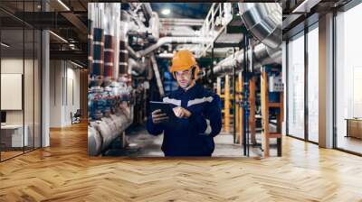 Portrait of young Caucasian man dressed in work wear using tablet while standing in heating plant. Wall mural