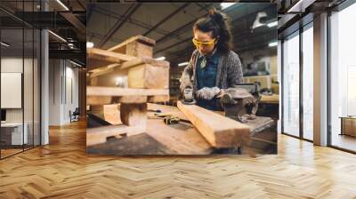 Portrait view of hardworking middle aged professional female carpenter worker working with sandpaper and choosing wood in the workshop. Wall mural