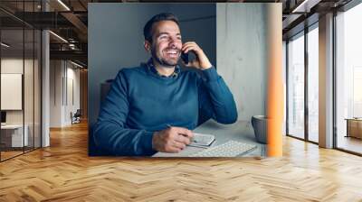 Remote job and work from home. A happy businessman is sitting at his home office, having a call with a client and writing down tasks. Wall mural