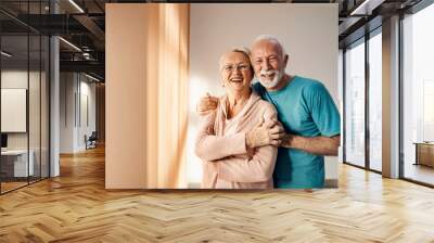 Senior couple hugging in a nursing home. A happy senior couple standing next to a window in a nursing home, hugging and smiling. They have all care they need. Wall mural