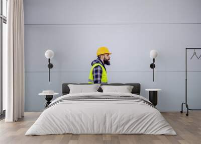 Side view of hardworking construction worker with safety helmet on head and in vest holding laptop in hands and rushing on construction site. Wall mural