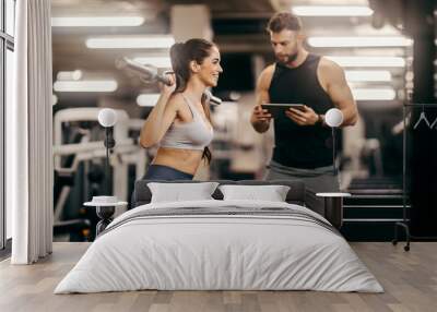 Side view of strong sportswoman practicing with weight bar at gym with her coach. Wall mural