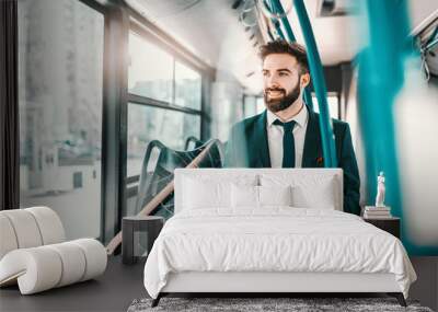 Smiling bearded Caucasian businessman in formal wear sitting in public transport and using smart phone. Wall mural