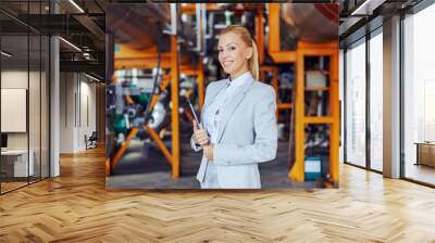 Smiling blond female CEO in formal wear standing in heating plant with tablet in hands. Wall mural