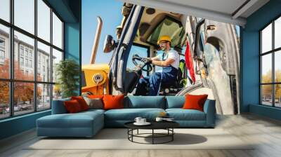 Smiling handsome caucasian worker in overall and with helmet on head driving excavator. Wall mural