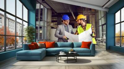 Smiling supervisor talking to construction worker about construction works. Worker holding blueprints and explaining to supervisor. Wall mural