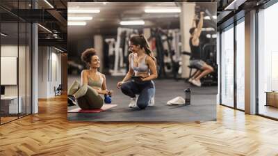 Sportswoman doing russian twist with kettlebell in a gym while her female fitness trainer is tracking progress on tablet. Wall mural