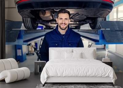 Technical inspection of cars and tablets. Man in uniform holds a tablet in his hands in the workshop canal in front of a car on a hydraulic elevator Portrait of a man at work in a workshop Car service Wall mural