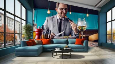 The man is about to take a bite of food, the man has lunch at a restaurant. A man elegantly dressed in a business suit eats and drinks in a restaurant. Business lifestyle, meals in restaurants Wall mural