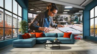 Thoughtful middle-aged industrial female engineer with eyeglasses working with a tape measure in the workshop. Wall mural