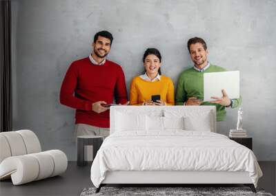 Three business people standing against the wall and holding various gadgets in hands. Wall mural