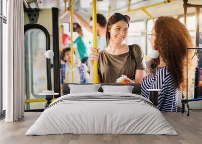 Two beautiful best friends are talking while standing in a bus full of people. Wall mural