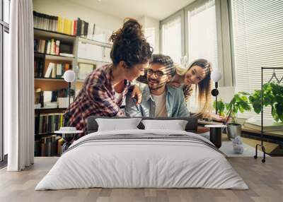 Two cheerful student girls helping their friend to pass the exam.Sitting in a bright library. Wall mural