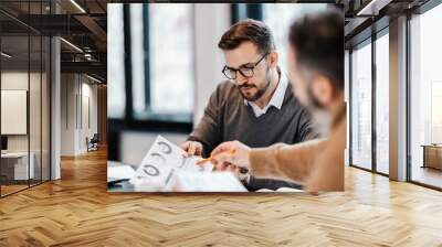 Two colleagues are sitting at the meeting room and discussing charts and statistics. Wall mural