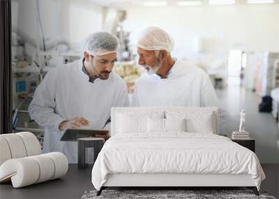 Worker holding casserole with cookies while supervisor checking quality and holding tablet. Food factory interior. Wall mural