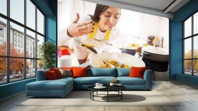 Young charming pretty woman is smiling while smelling the aroma of her fresh healthy breakfast being cooked. Wall mural