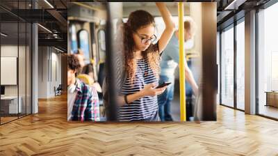 Young cute girl is standing in bus and checking messages on her phone. Wall mural