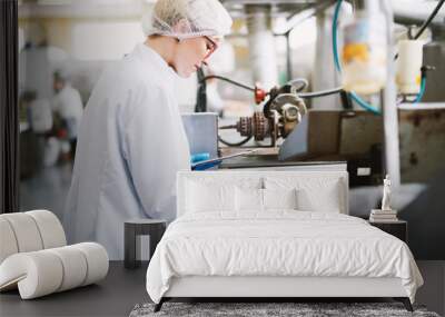 Young female worker in sterile clothes is taking a sample of salt snacks from production line. Wall mural