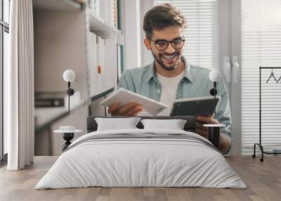 young smiling mixed race male student using tablet to find book he need for studying. library interi Wall mural