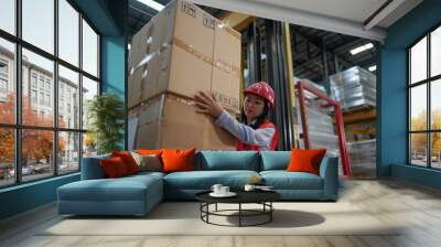 an attractive Asian logistics warehouse staff girl wearing red safety helmet red warehouse vest is moving a big cardboard box with a Platform trucks, inside huge neat warehouse,. Wall mural