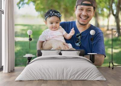 Happy Asian father holding a cute little baby girl on blured background of green garden,  father looking at camera Wall mural