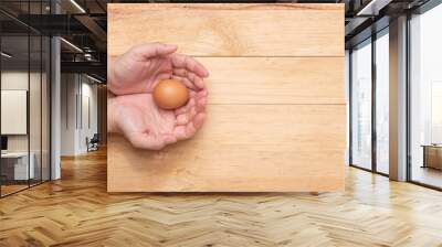 Top view of two hands holding a raw chicken egg on a light brown wooden background, copy space Wall mural