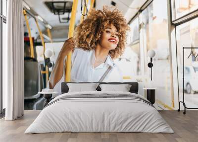 Beautiful and fashionable black woman standing in city bus. She is happy and smiled. Modern city lifestyle concept. Bright sunny day. Wall mural