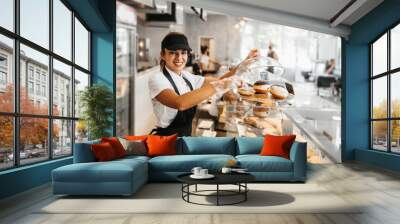 Beautiful young and happy female worker working in a modern bakery or fast food restaurant. Wall mural