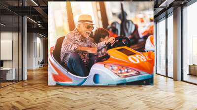 Grandfather and grandson having fun and spending good quality time together in amusement park. They enjoying and smiling while driving bumper car together. Wall mural