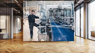 Happy smiled worker doing his job on Robotic factory line for processing and quality control of pure spring water bottled into canisters. Low light and small amount of noise visible.  Wall mural