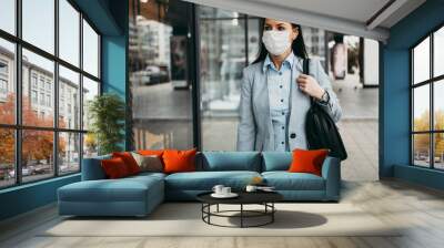 Young and elegant business woman with face protective mask standing on empty street and looking at storefront of closed store. Corona virus or Covid-19 concept. Wall mural