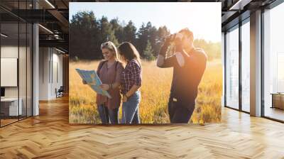 young friends enjoying outdoor. two girls standing in deep grass, smiling and looking at map to find Wall mural