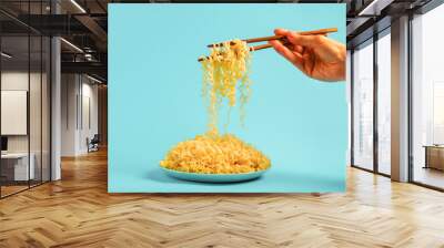 Egg noodles on blue plate and female hands with chopsticks on blue background Wall mural