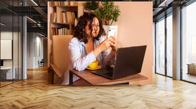 Young woman using laptop and mobile phone at the working space. Wall mural