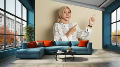 Young asian muslim woman wearing hijab smiling confident pointing with fingers to different directions. Copy space for advertisement
 Wall mural