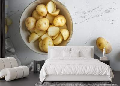 A bowl of potatoes sits on a table, with peels and a kitchen towel next to it. A knife lies nearby. Wall mural