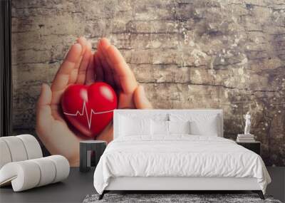 Top view of two hands holding a red heart with a pulse line, a health care concept. Wall mural