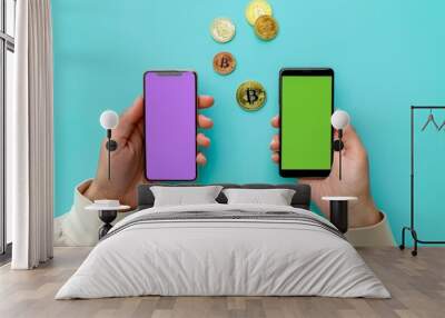 Two hands holding mobile phones, one with a purple screen and the other with a green screen, with three golden coins floating in front. Wall mural