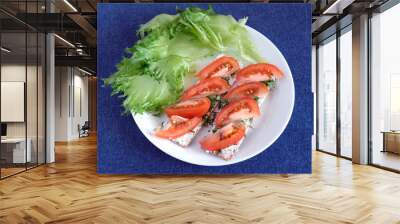 Tasty healthy low calorie vegetarian food with two small load of bread with cutted fresh tomatoes on cottage cheese and green salad leaves on round white plate over blue denim tablecloth top view Wall mural